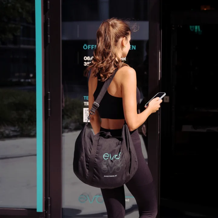 Woman with EVO gym bag entering EVO Fitness, holding phone