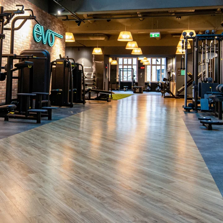 EVO Fitness interior with wood flooring, strength machines, neon logo, and warm lighting