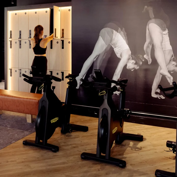 Woman at locker in EVO Fitness beside spin bikes and large wall mural